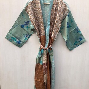 May include: A long, flowing robe in shades of teal, brown, and cream, with a patterned design. The robe features a matching belt and is displayed on a wooden hanger. The sleeves have a geometric pattern in blue and teal.