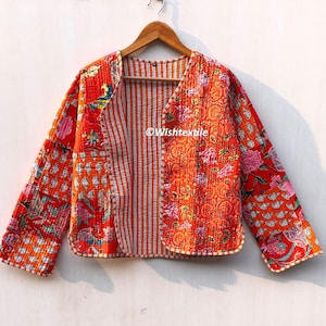 May include: A bright orange and white quilted jacket with a floral print and striped fabric. The jacket has a V-neck and long sleeves. The text "Wishtextile" is visible on the front of the jacket.