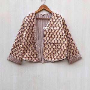 May include: A cream-coloured quilted jacket with a red and white striped lining. The jacket has a floral print and a V-neck.