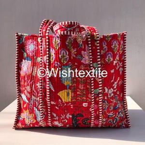 Könnte beinhalten: Eine gesteppte Tragetasche aus leuchtend rotem Stoff mit einem mehrfarbigen Blumenmuster. Die Tasche hat zwei stabile Griffe und Kanten, die mit einem weiß-rot gestreiften Stoff eingefasst sind. Der Text Wishtextile ist mittig aufgedruckt.