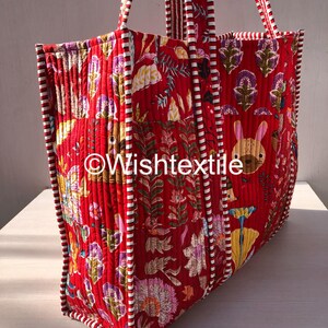 May include: A quilted tote bag in a vibrant red fabric featuring a repeating pattern of stylised flowers, leaves, and a small rabbit. The bag has red and white striped fabric trim along the edges and handles. The text Wishtextile is visible.