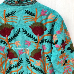 May include: A turquoise blue jacket with intricate floral embroidery in shades of orange, pink, green, and red. The embroidery features stylized flowers and leaves.