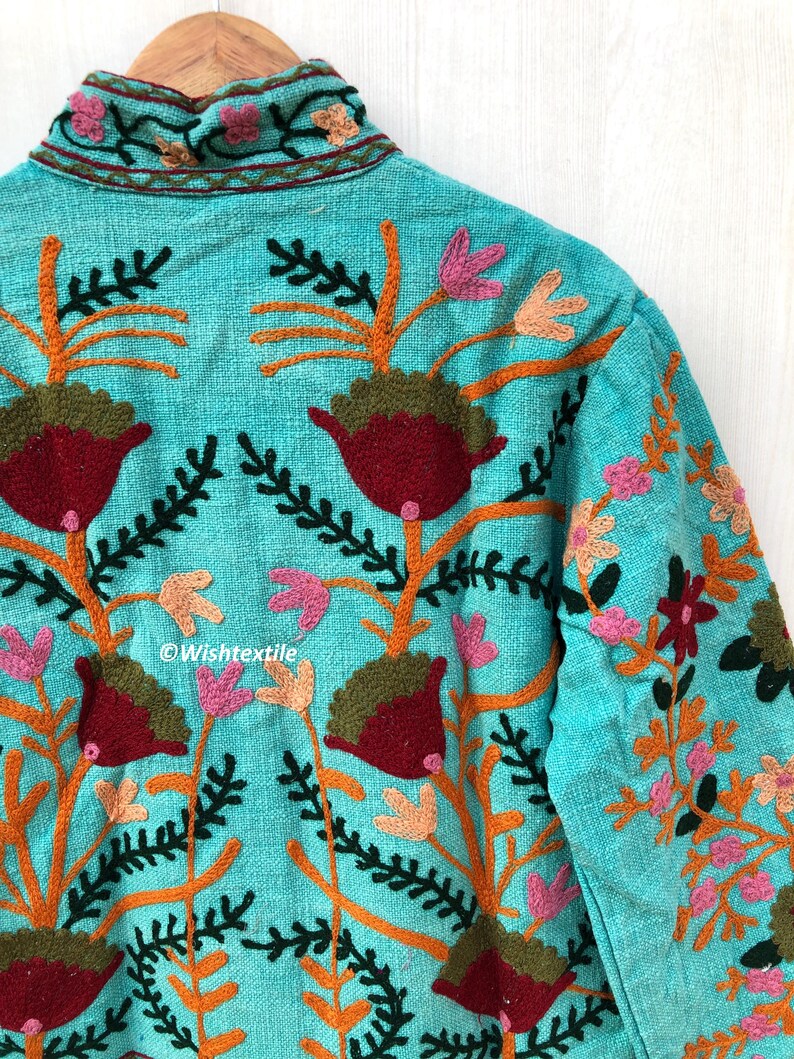 May include: A turquoise blue jacket with intricate floral embroidery in shades of orange, pink, green, and red. The embroidery features stylized flowers and leaves.