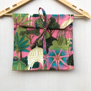 Pu&ograve; includere: Una borsa regalo in tessuto rosa con un design a fantasia verde, blu e bianco con alberi, pavoni e cupole. La borsa &egrave; legata con un nastro rosa.