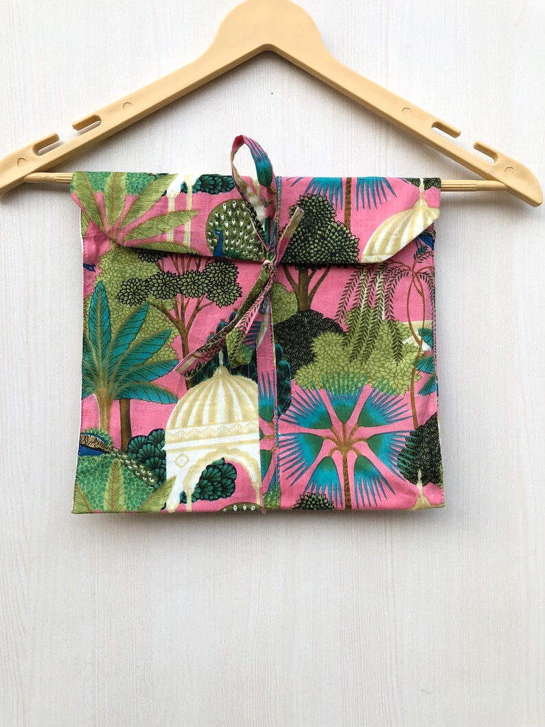 Pu&ograve; includere: Una borsa regalo in tessuto rosa con un design a fantasia verde, blu e bianco con alberi, pavoni e cupole. La borsa &egrave; legata con un nastro rosa.
