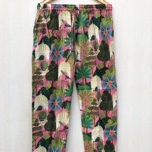 Pu&ograve; includere: Pantaloni da pigiama rosa con stampa bianca, verde e blu di alberi, pavoni ed edifici. I pantaloni hanno una vita con coulisse e un bordo bianco.