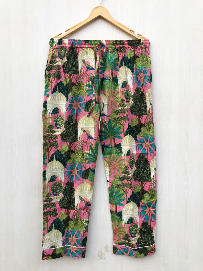 Pu&ograve; includere: Pantaloni da pigiama rosa con stampa bianca, verde e blu di alberi, pavoni ed edifici. I pantaloni hanno una vita con coulisse e un bordo bianco.