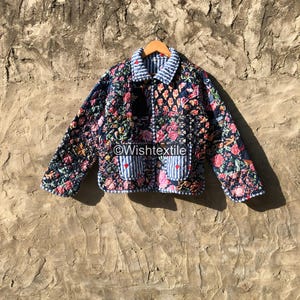 Könnte beinhalten: Eine gesteppte Jacke mit dunkelblauer Basis und einem lebendigen Blumenmuster in Pink, Rot und Grün. Das Kleidungsstück verfügt über einen blau-weiß gestreiften Kragen und zwei Vordertaschen mit passenden Streifen. Der Text Wishtextile ist sichtbar.
