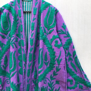 May include: A purple robe with green floral embroidery. The robe features a long, open front design with a striped lining. The sleeves are long, and the embroidery covers the front and sleeves.
