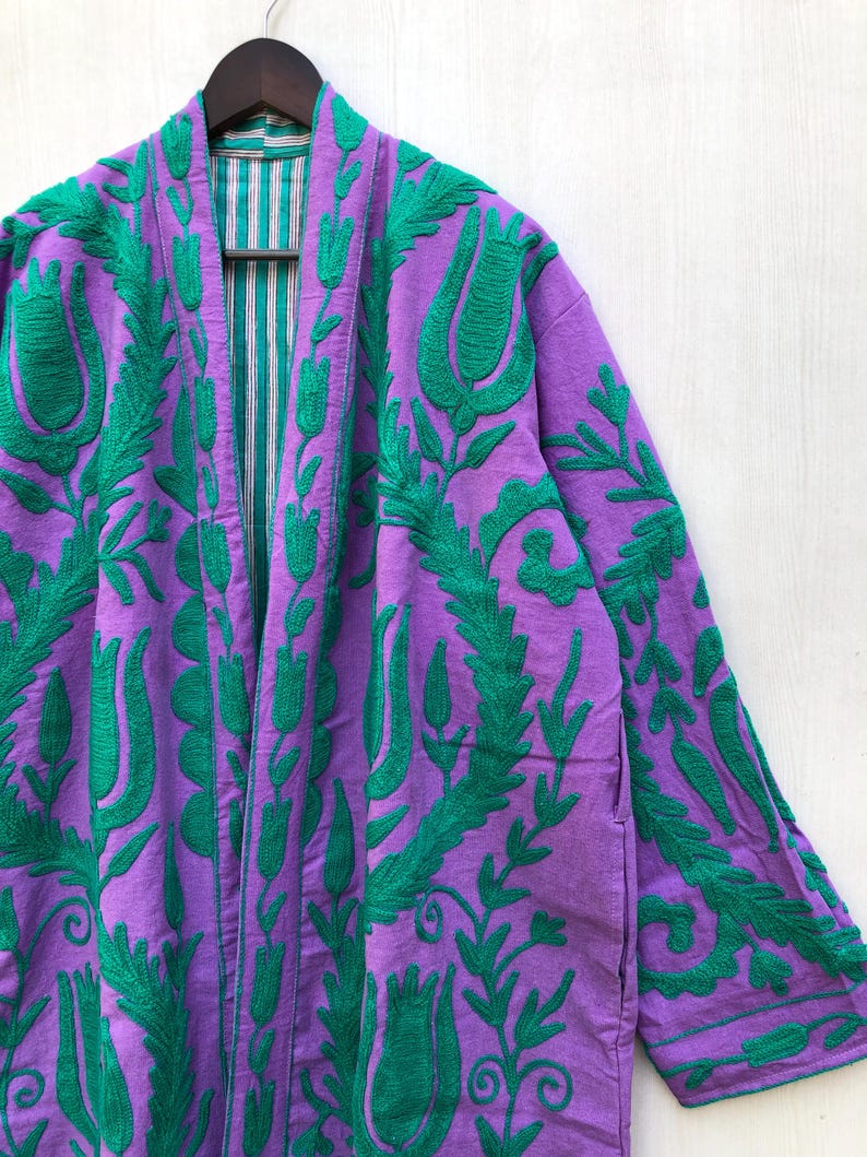 May include: A purple robe with green floral embroidery. The robe features a long, open front design with a striped lining. The sleeves are long, and the embroidery covers the front and sleeves.