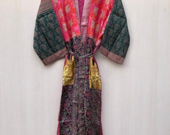 May include: A long, pink silk robe with a patchwork design. The robe has a green, pink, and orange floral pattern on the sleeves and a gold and black floral pattern on the bottom. The robe has a sash tie at the waist.
