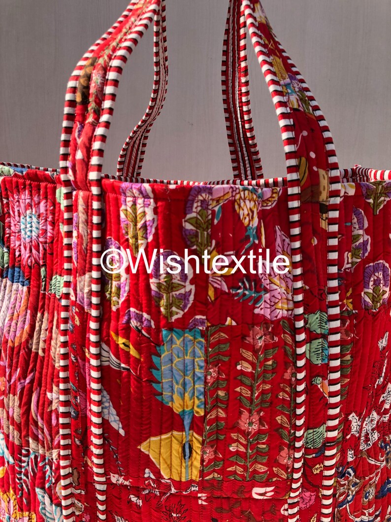 May include: A quilted tote bag featuring a vibrant red base with a multi-coloured floral and botanical print. The bag includes two sturdy handles with a red and white striped pattern. The text @Wishtextile is printed in white across the centre.