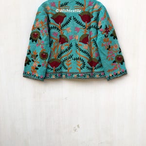 May include: A turquoise blue jacket with a high neck and long sleeves. The jacket is embroidered with colorful floral designs and the text "@Wishtextile".