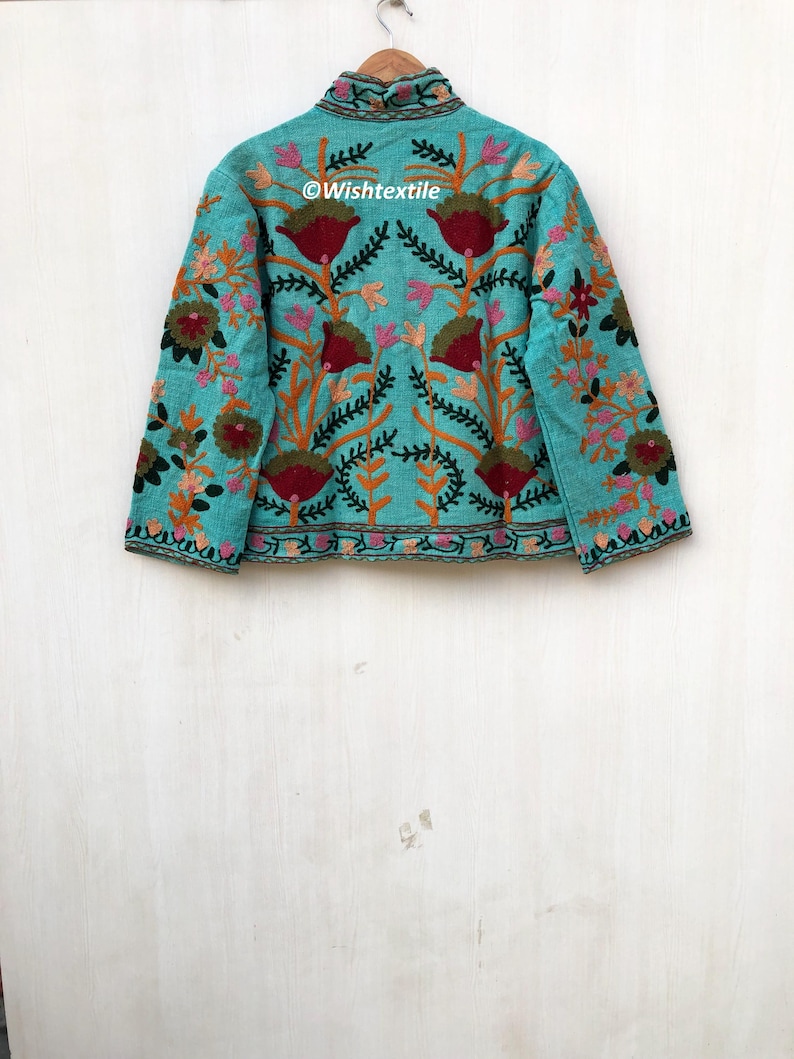 May include: A turquoise blue jacket with a high neck and long sleeves. The jacket is embroidered with colorful floral designs and the text "@Wishtextile".