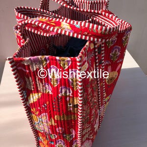 May include: A quilted tote bag featuring a vibrant red background with a multi-coloured floral and animal print. The bag has red and white striped fabric trim along the edges and handles. The text "&copy;Wishtextile" is printed on the side of the bag.