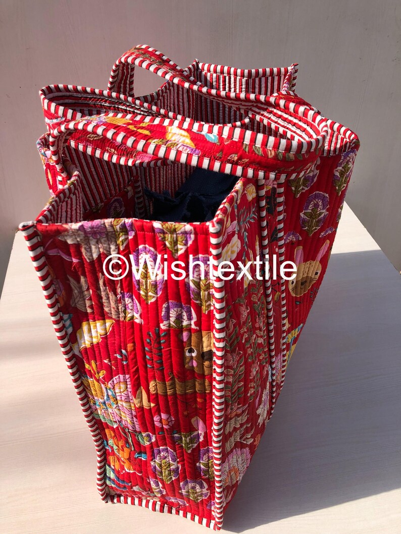 May include: A quilted tote bag featuring a vibrant red background with a multi-coloured floral and animal print. The bag has red and white striped fabric trim along the edges and handles. The text "&copy;Wishtextile" is printed on the side of the bag.
