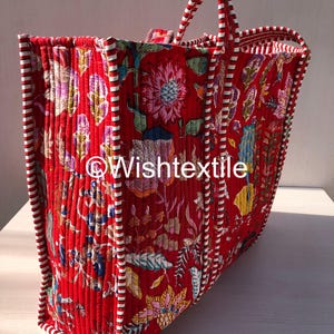 May include: A quilted tote bag featuring a vibrant red base with a multi-coloured floral pattern. The bag has white and red striped fabric trim along the edges and handles. The text "Wishtextile" is printed in white across the centre of the bag.