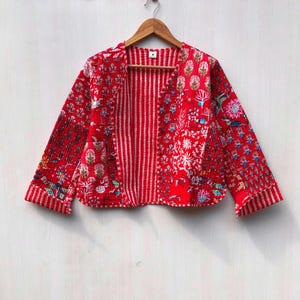 Peut inclure: Veste matelassée rouge avec des motifs floraux et géométriques. L'intérieur de la veste est rayé et elle est présentée sur un cintre en bois. L'extérieur de la veste présente divers motifs floraux et botaniques colorés.