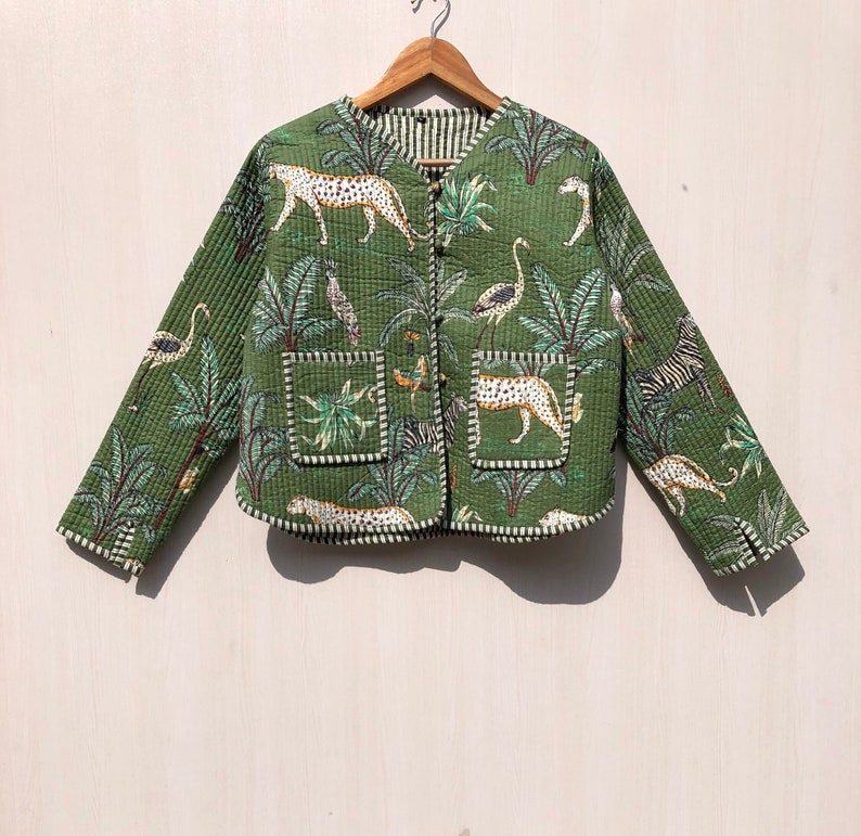 May include: A green quilted jacket with a safari print featuring zebras, leopards, and palm trees. The jacket has a button closure and two patch pockets.