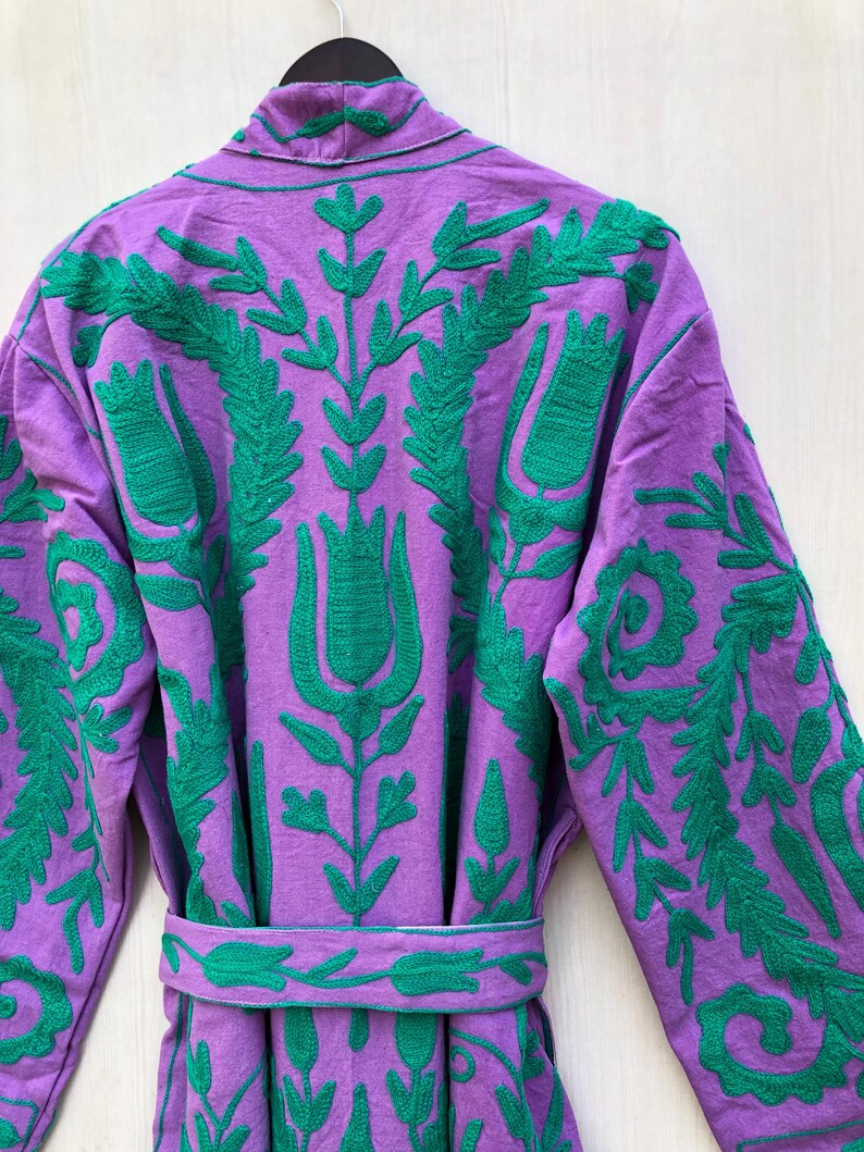 May include: A purple robe with green floral embroidery. The robe features a shawl collar, long sleeves, and a matching belt. The embroidery is detailed and covers the back and sleeves of the robe.