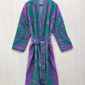 May include: A purple robe with green floral embroidery and a matching belt hangs on a wooden hanger. The robe's interior features a striped pattern. The embroidery covers the sleeves, lapels, and front panels, creating a striking visual contrast.