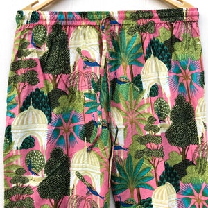 Pu&ograve; includere: Pantaloni da pigiama rosa con una stampa colorata di pavoni, alberi ed edifici bianchi. I pantaloni hanno una cintura elastica e un cordoncino.