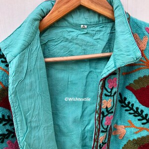 May include: A turquoise blue embroidered jacket with floral and leaf designs in shades of pink, red, orange, and green. The jacket has a collar and a button closure. The size tag says "XL".