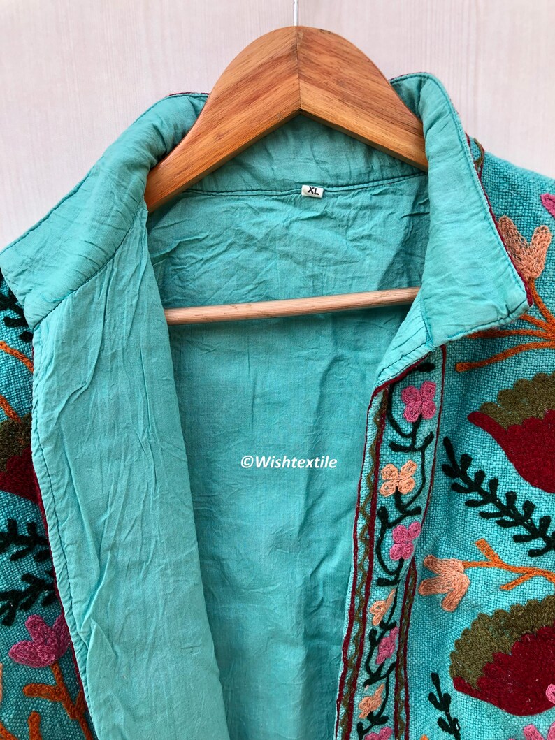 May include: A turquoise blue embroidered jacket with floral and leaf designs in shades of pink, red, orange, and green. The jacket has a collar and a button closure. The size tag says "XL".