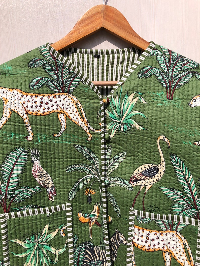 May include: A green quilted vest with a jungle print featuring leopards, flamingos, zebras, and palm trees. The vest has a striped lining and two pockets.