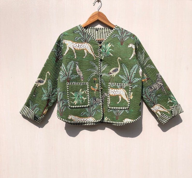 May include: A green quilted jacket with a jungle print featuring leopards, zebras, flamingos, and palm trees. The jacket has a button closure and two pockets.