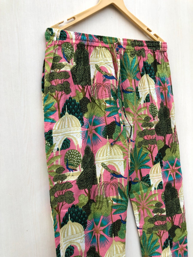 Pu&ograve; includere: Pantaloni rosa con una stampa colorata di pavoni, alberi ed edifici. I pantaloni hanno una cintura elastica e un cordoncino.