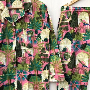 Pu&ograve; includere: Un pigiama rosa e verde con una stampa di pavoni, alberi ed edifici. Il set comprende una camicia a maniche lunghe e pantaloni.