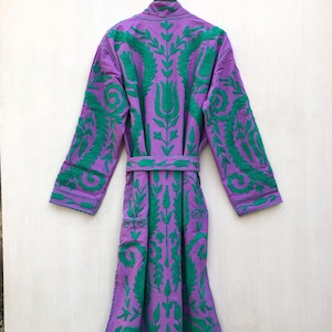 May include: A purple robe with green embroidered floral patterns. The robe has long sleeves and a matching belt. The embroidery is detailed and covers the front, back, and sleeves of the robe. The robe is hanging on a black hanger.