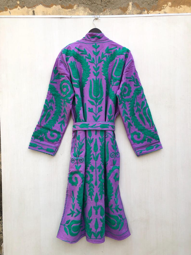 May include: A purple robe with green embroidered floral patterns. The robe has long sleeves and a matching belt. The embroidery is detailed and covers the front, back, and sleeves of the robe. The robe is hanging on a black hanger.