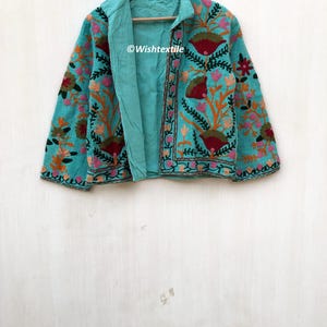 May include: A teal blue embroidered jacket with floral patterns in shades of pink, orange, green, and red. The jacket has a collar and long sleeves. The text "@Wishtextile" is visible on the jacket.