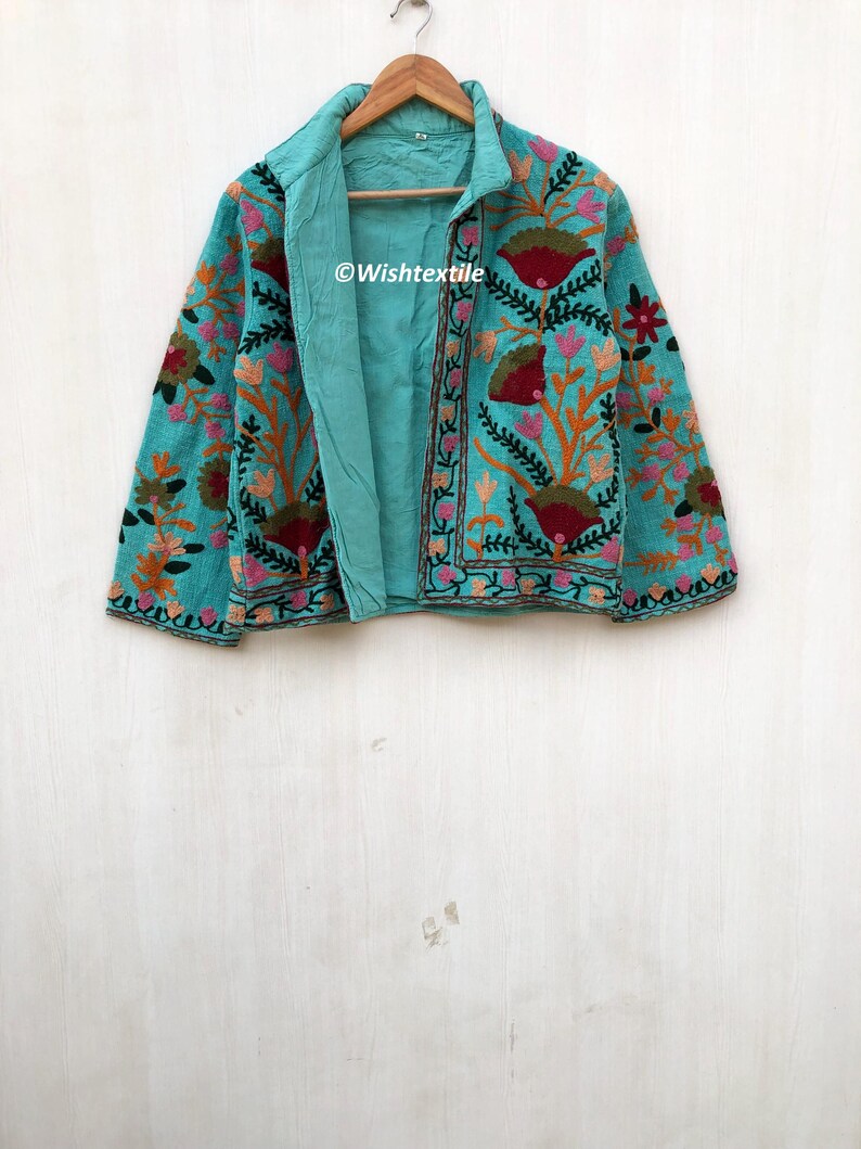 May include: A teal blue embroidered jacket with floral patterns in shades of pink, orange, green, and red. The jacket has a collar and long sleeves. The text "@Wishtextile" is visible on the jacket.