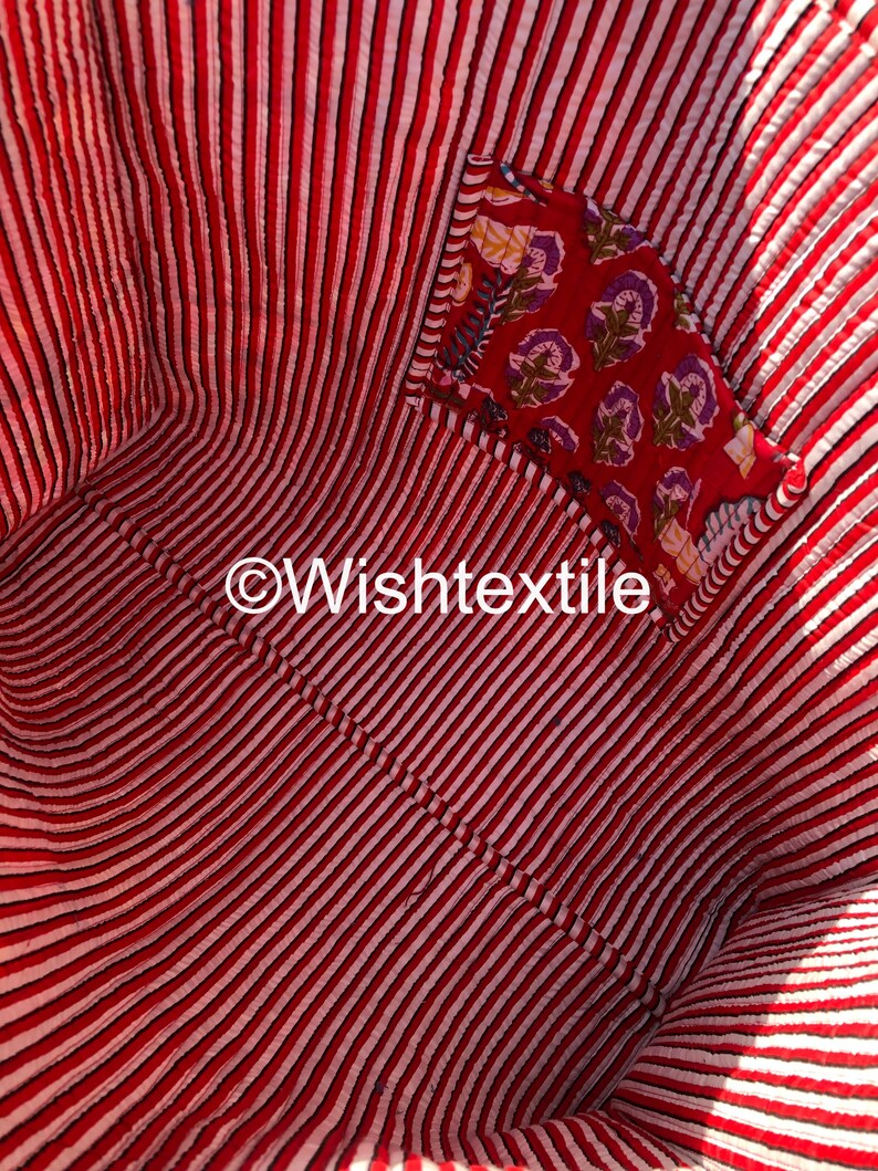 May include: The interior of a quilted fabric bag featuring a red and white vertical striped pattern. An internal pocket is attached to the side, showcasing a red fabric with a floral print in purple and yellow. The text Wishtextile is visible.