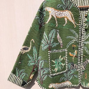 May include: A green quilted jacket with a jungle print featuring leopards, zebras, birds, and palm trees. The jacket has a white and green striped lining and a white and green striped pocket.