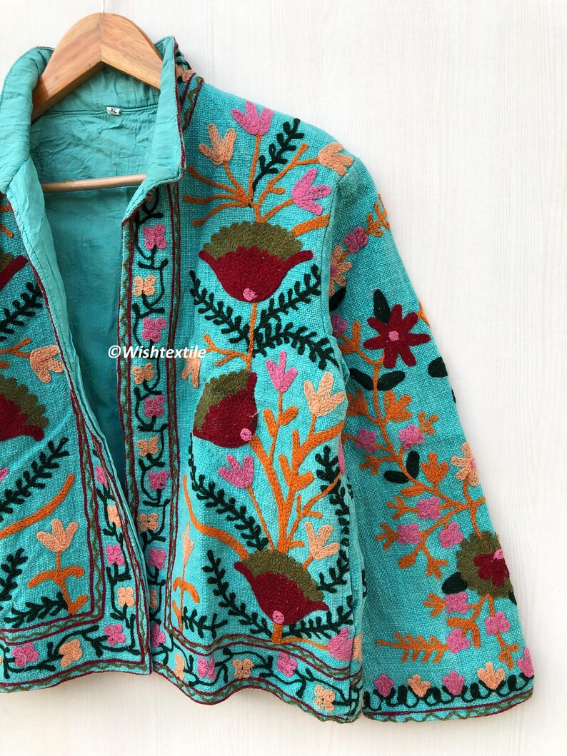 May include: A turquoise blue jacket with floral embroidery in shades of pink, orange, green, and red. The jacket has a collar and a button closure.
