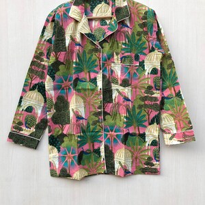 Pu&ograve; includere: Una camicia a maniche lunghe rosa e verde con una stampa paisley che presenta pavoni e alberi. La camicia ha una chiusura con bottoni sul davanti e un bordo bianco.