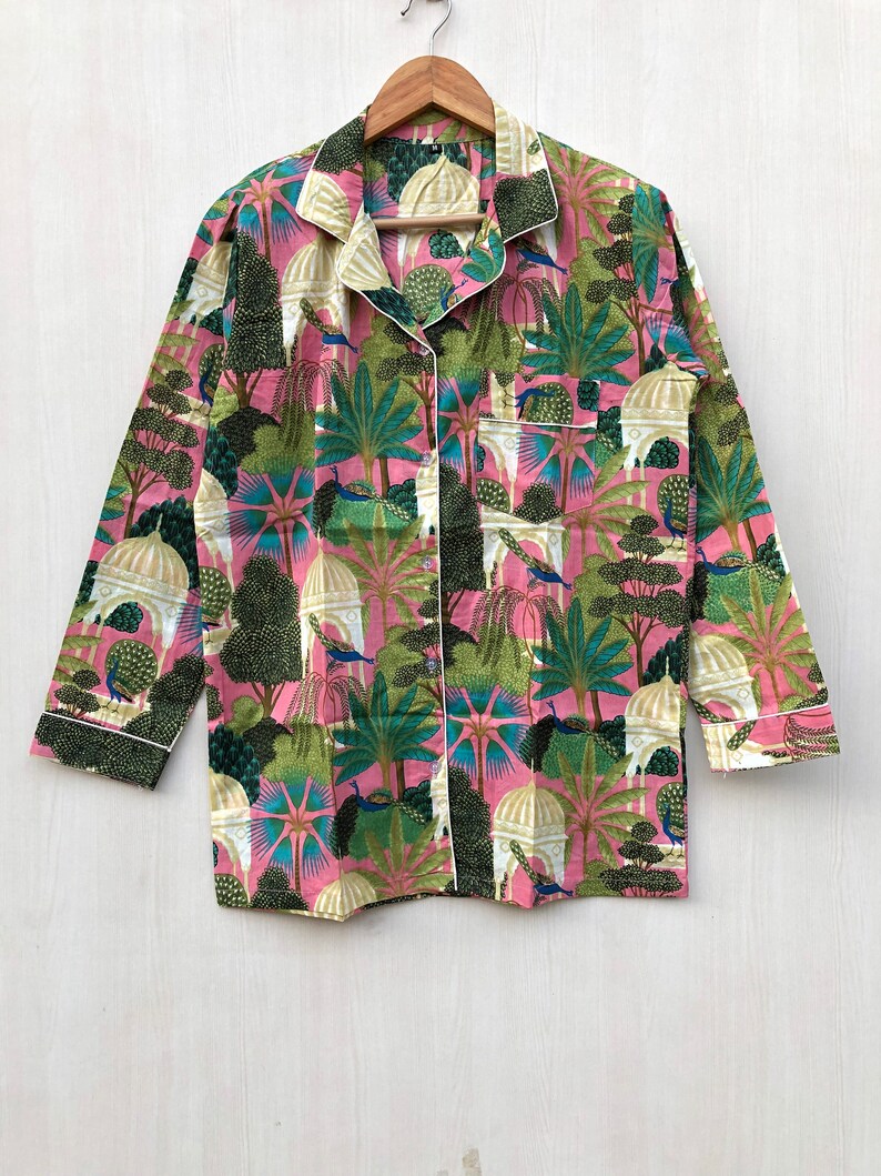 Pu&ograve; includere: Una camicia a maniche lunghe rosa e verde con una stampa paisley che presenta pavoni e alberi. La camicia ha una chiusura con bottoni sul davanti e un bordo bianco.