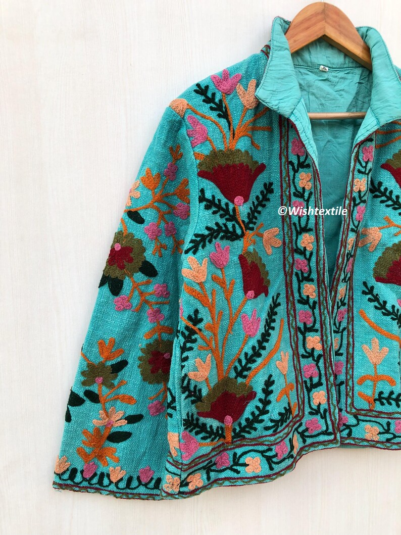 May include: A turquoise blue jacket with a floral embroidery design. The jacket has a collar and a front closure. The embroidery is in shades of pink, red, orange, green, and brown. The text "@Wishtextile" is visible on the jacket.
