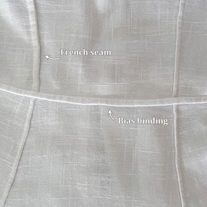 May include: Close-up of a white fabric garment with a French seam and bias binding. The seam is visible on the top and the binding is visible on the bottom.