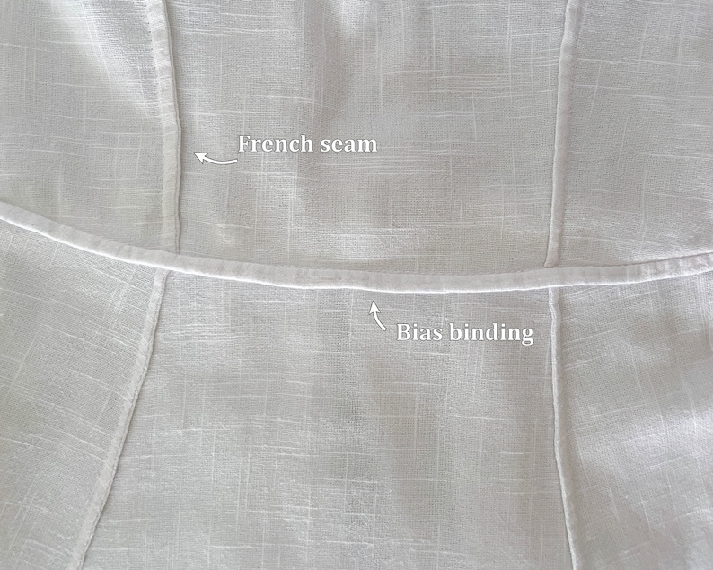 May include: Close-up of a white fabric garment with a French seam and bias binding. The seam is visible on the top and the binding is visible on the bottom.