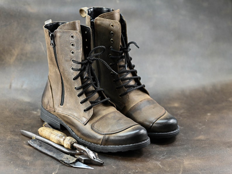 May include: A pair of brown leather boots with black laces and a zipper on the side. The boots are sitting on a brown surface with a small tool next to them.