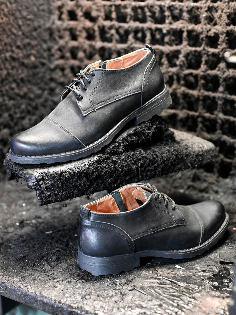 May include: Two pairs of black leather lace-up shoes with a cap toe design. The shoes are on a dark surface.