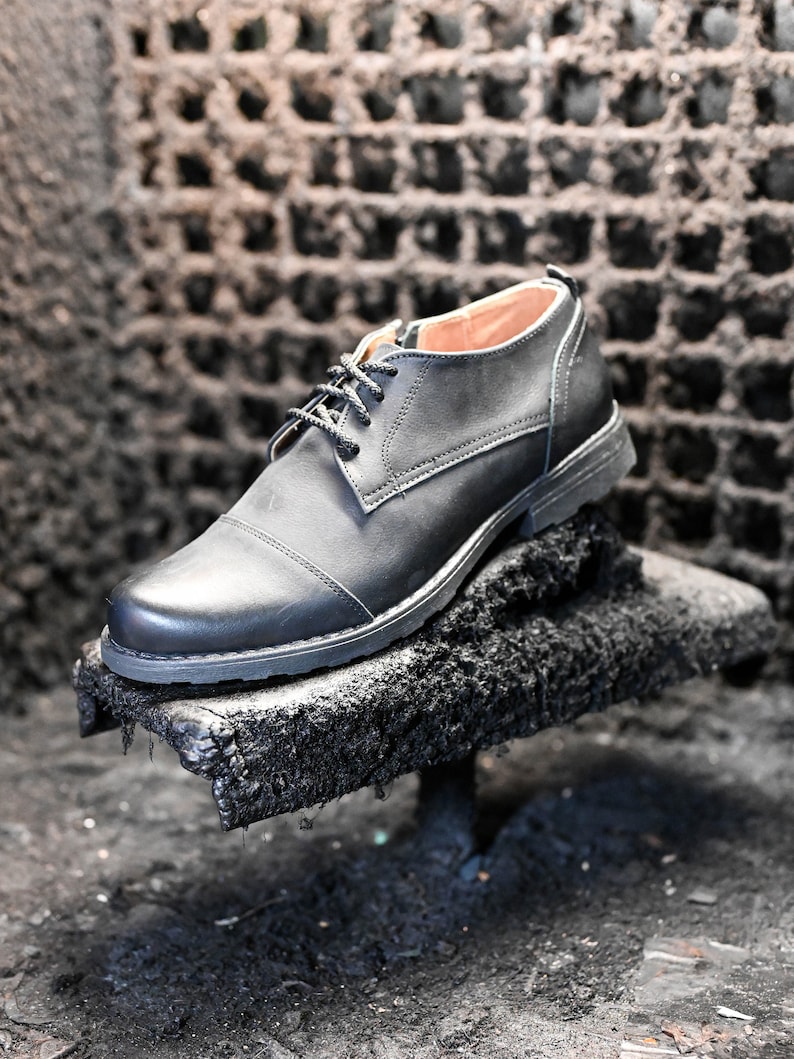 May include: A black leather oxford shoe with a lace-up closure. The shoe is sitting on a rough, black surface.