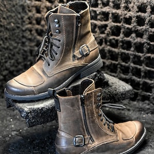 May include: A pair of brown leather boots with black laces and a zipper on the side. The boots have a buckle strap and a rugged sole.