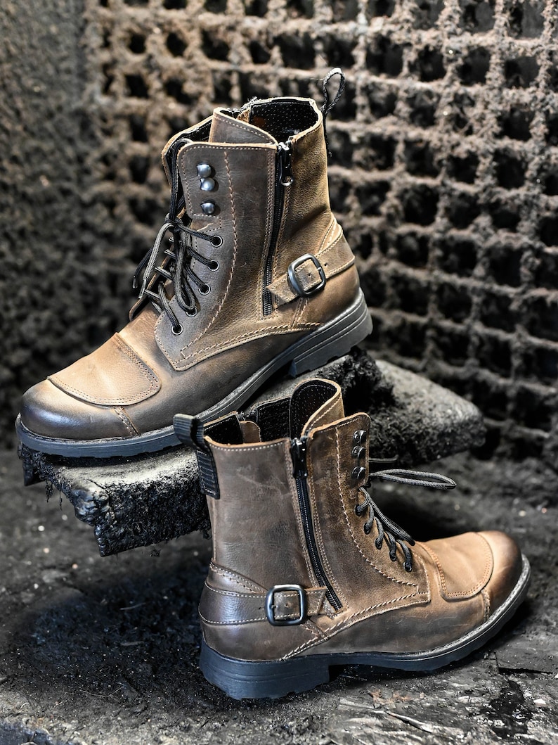 May include: A pair of brown leather boots with black laces and a zipper on the side. The boots have a buckle strap and a rugged sole.