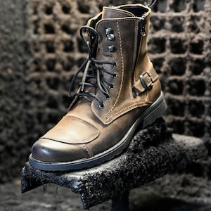 May include: A brown leather ankle boot with black laces and a zipper on the side. The boot has a buckle on the side and a thick black sole.